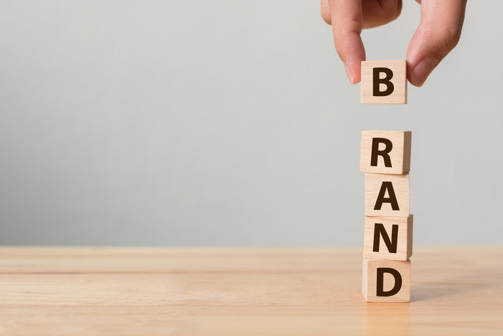 Hand of male putting wood cube block with word “BRAND” on wooden table. Brand building for success concept